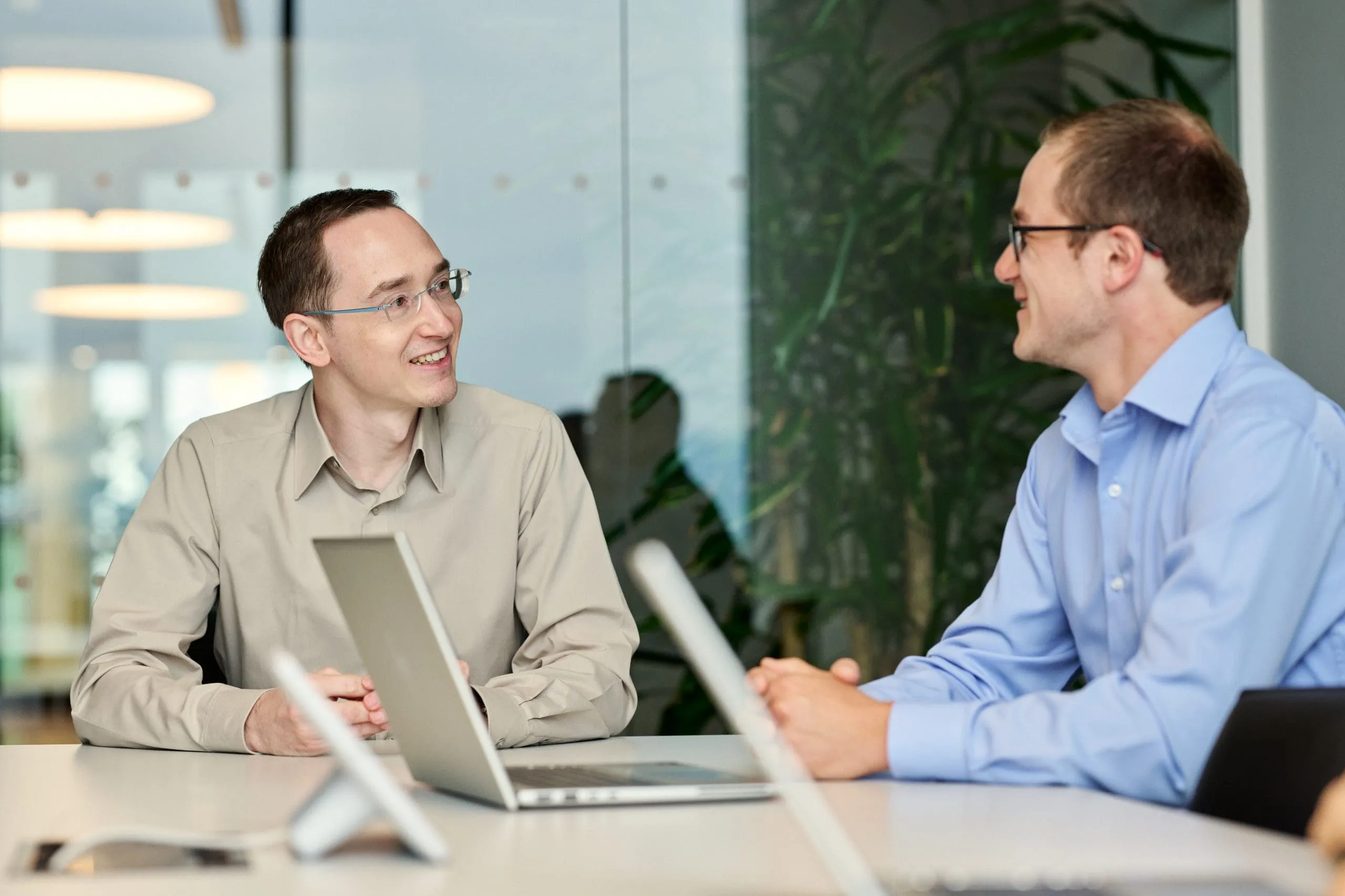 Three professionals, two men and one woman, sit around a conference table in a bright office space, smiling and engaged in conversation. image