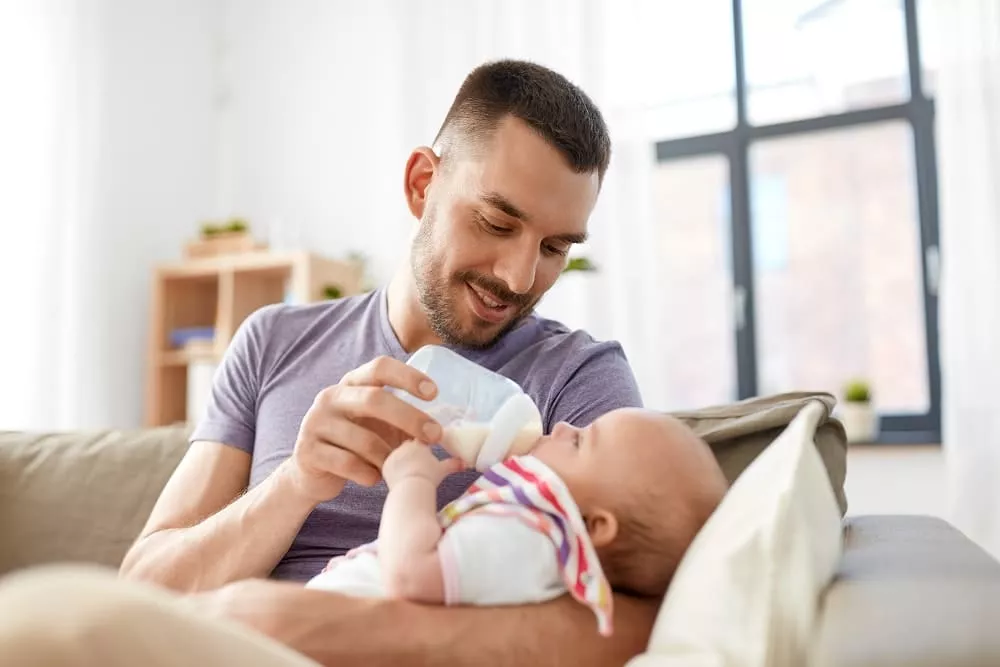 Smiling man feeding a baby with a bottle while holding them in his arms. image