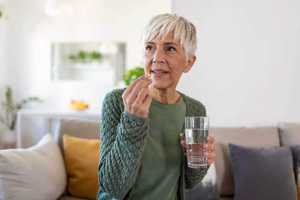 Senior woman takes pill with glass of water in hand. image