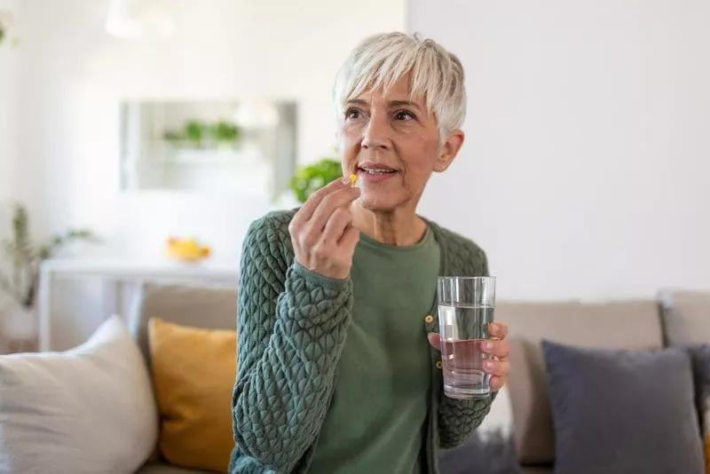 Senior woman takes pill with glass of water in hand.