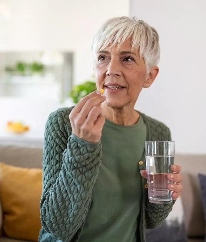Senior woman takes pill with glass of water in hand.