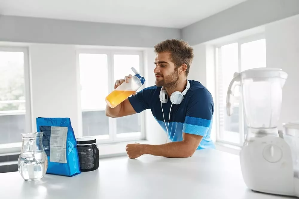 Man in sportswear holding a shaker bottle with orange drink in a bright kitchen. image