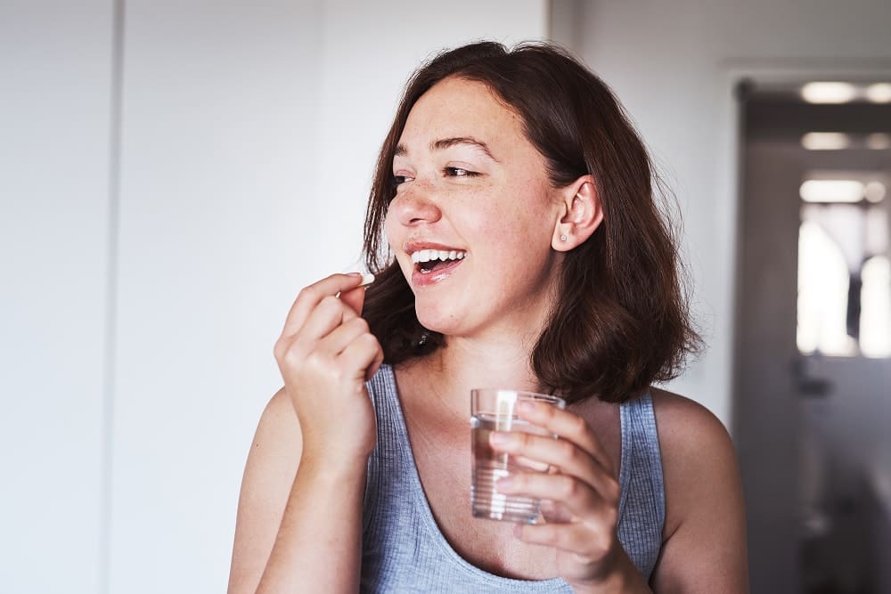 Smiling woman holding a glass of water and about to take a pill.