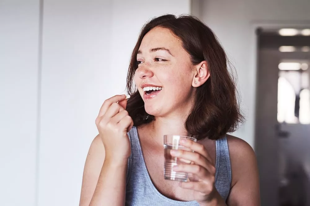Smiling woman holding a glass of water and about to take a pill.