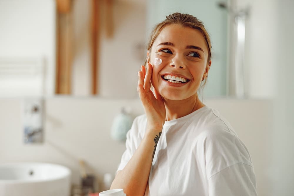 Woman smiling and applying moisturiser to her face.