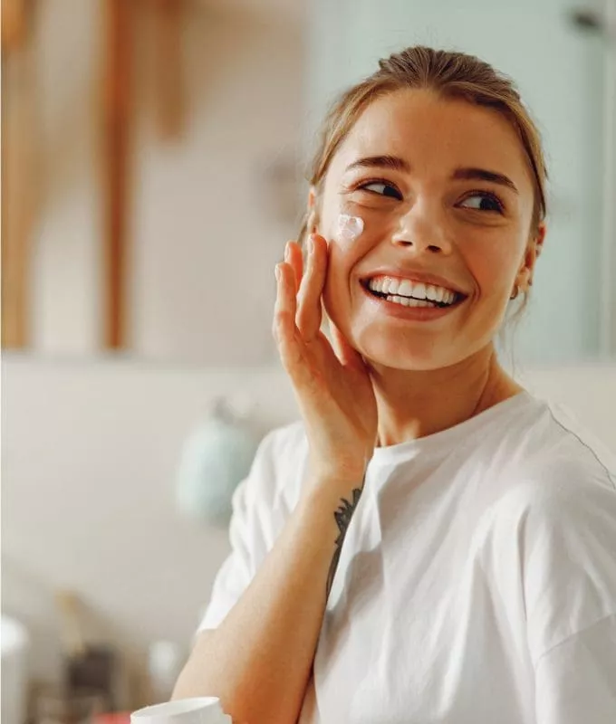 Woman smiling and applying moisturiser to her face.