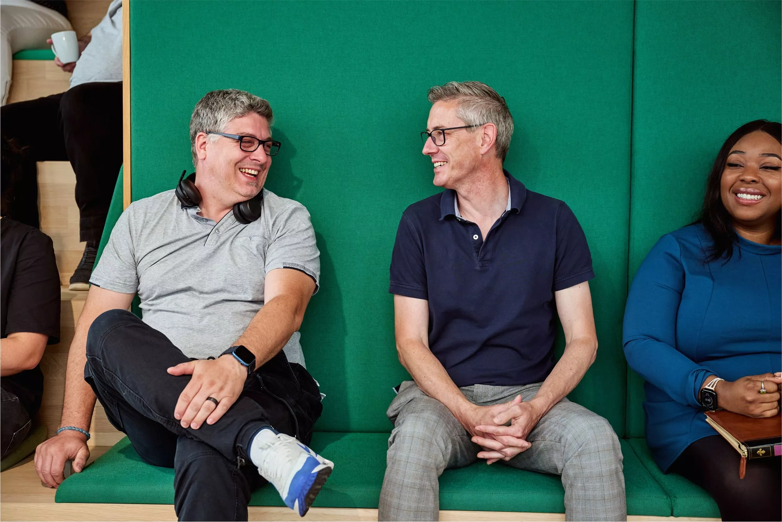 Three colleagues sitting on a green bench, smiling and chatting. image