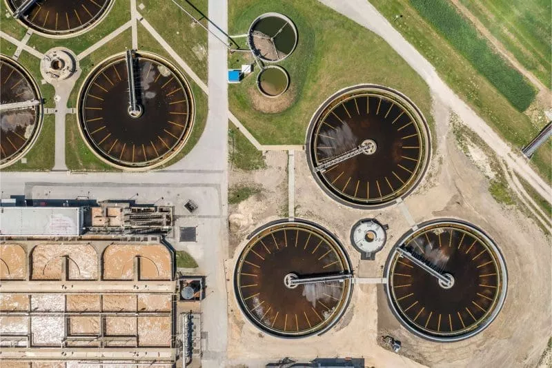 Aerial view of a wastewater treatment plant showing multiple circular clarifiers and rectangular processing tanks.